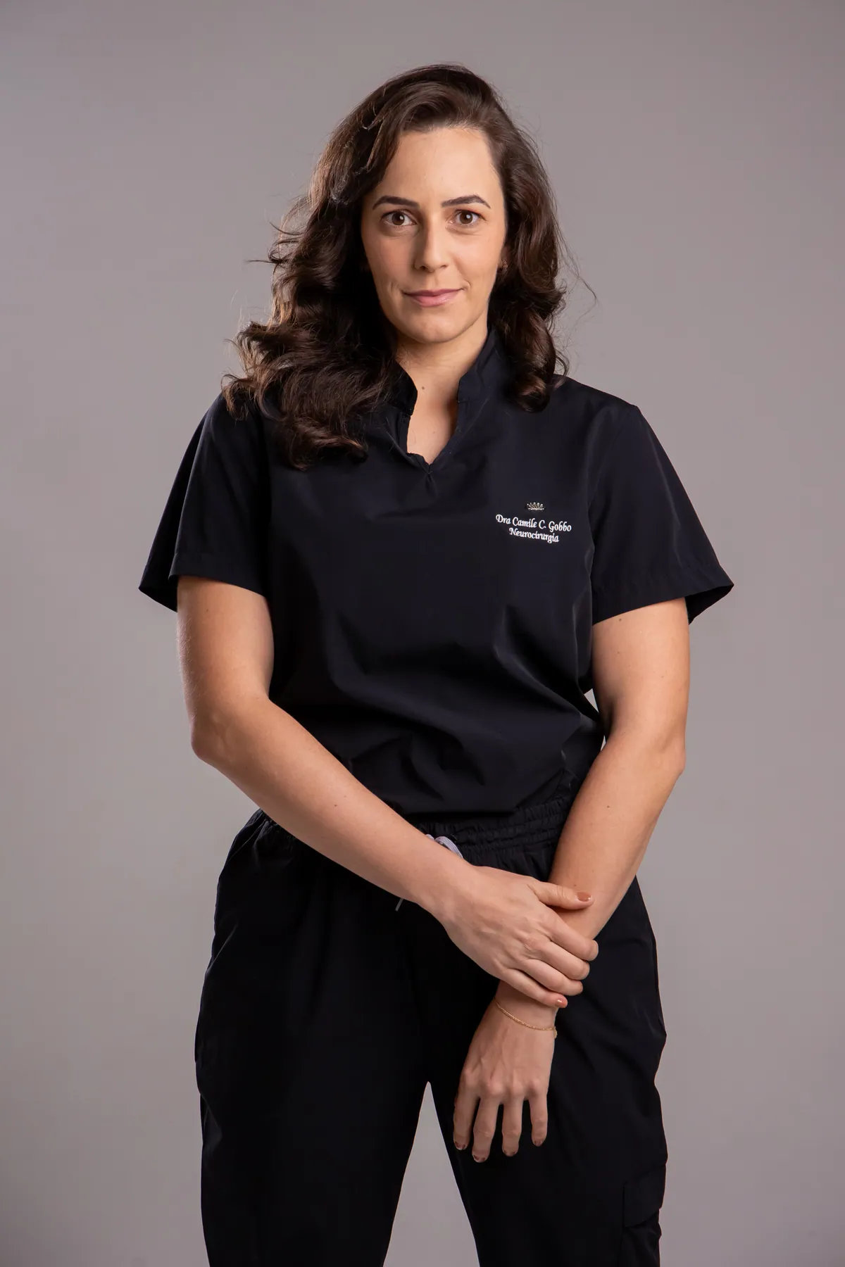 Dra. Camile C. Gobbo em jaleco cirúrgico bordado com seu nome e a especialidade Neurocirurgia
